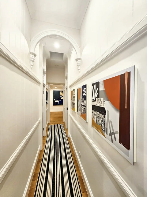 Narrow hallway with arched ceiling, striped runner, and modern artwork on walls.