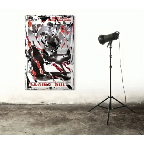 Abstract painting with black, white, and red splatters and text, displayed next to a standing spotlight.