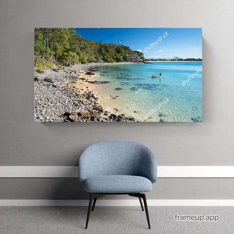 Coastal beach landscape artwork mounted above a gray upholstered accent chair.